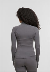 En kvinna visar baksidan av en grå, långärmad och figurnära träningsjacka.