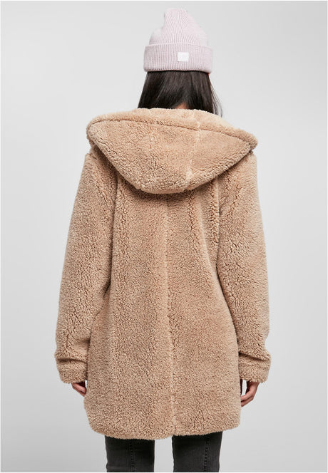 En kvinna fotograferad bakifrån i en beige sherpajacka med huva och en rosa mössa.